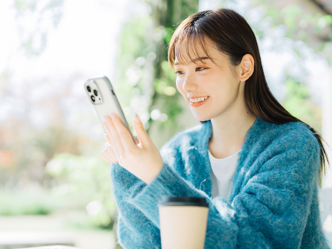 手に持つスマホ画面を見て微笑んでいる女性の写真